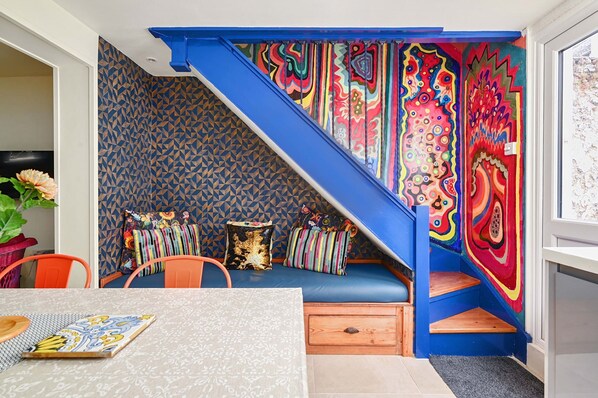 A room with a blue staircase, colorful wall art, a blue sofa with cushions, and a dining table with a patterned table runner. - Host Stay Foundry Colours (Brighton)