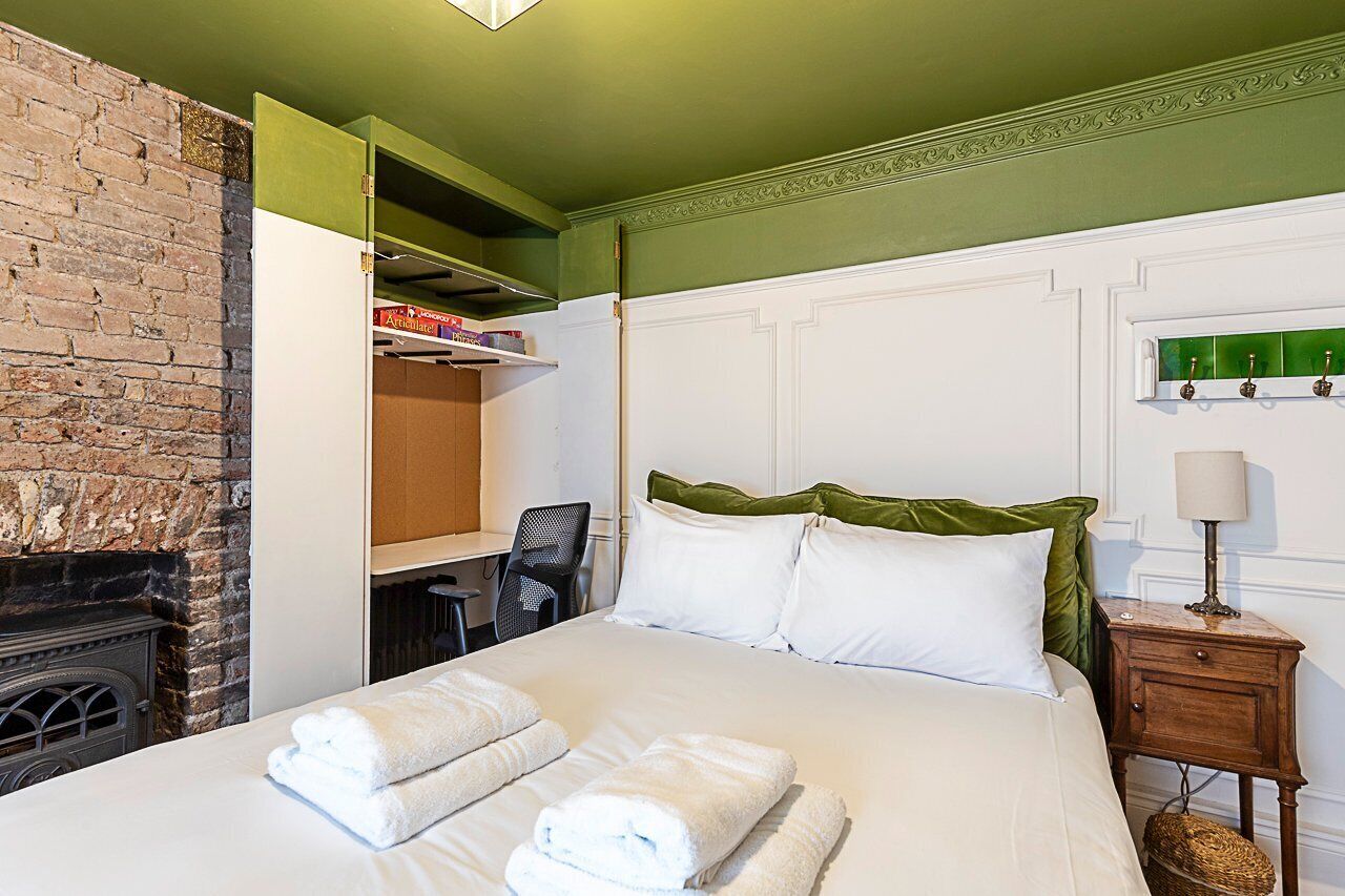 A hotel room with a bed, a fireplace, a desk, and a green accent wall.