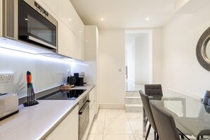 A modern kitchen with a microwave, coffee maker, and toaster. There is a dining area with a glass table and chairs.