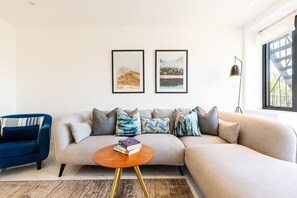 A modern living room with a sectional sofa, a blue armchair, a round coffee table, and two framed pictures on the wall.