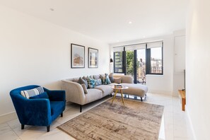 A modern living room with a sofa, armchair, and coffee table, large windows, and a view of the city.