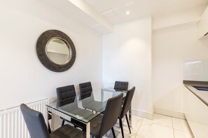A modern kitchen with a white countertop, a black circular mirror, and a glass dining table with four chairs. - Elegant Three-Bed Marylebone Flat Near Oxford Circus! (London)