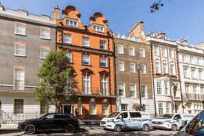 A row of multi-story buildings with a mix of brick and stone facades, a tree in the foreground, and parked cars including a white van with 'evolution' branding.