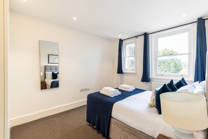A hotel room with a bed, a bedside lamp, a window with curtains, a mirror, and a view of the outside.