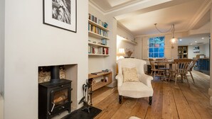A cozy living room with a fireplace, bookshelves, a dining area with a table and chairs, and a view of the kitchen through an open window. - Host Stay The September Cottage (Brighton)
