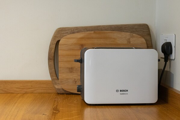 A white Bosch ComfortLine portable heater with a power cord plugged into a wall socket, placed on a wooden floor next to a wooden wall. - Host Stay The September Cottage (Brighton)