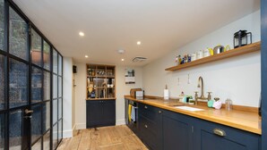 A modern kitchen with dark cabinets, a wooden countertop, and a large window. - Host Stay The September Cottage (Brighton)
