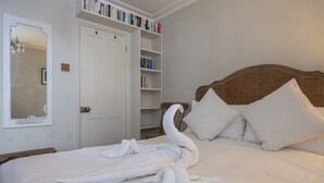 A neatly made bed with a swan-shaped towel arrangement, a wooden headboard, and a bookshelf with books. - Host Stay The September Cottage (Brighton)