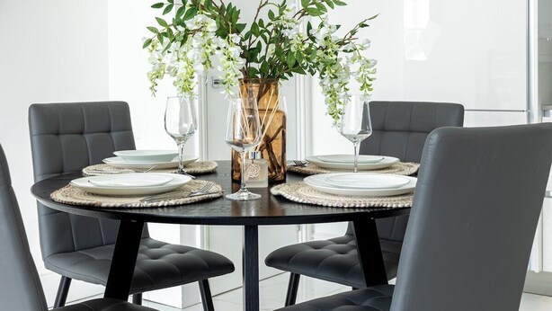 Een ronde eettafel met vier stoelen, een vaas met witte bloemen en wijnglazen.