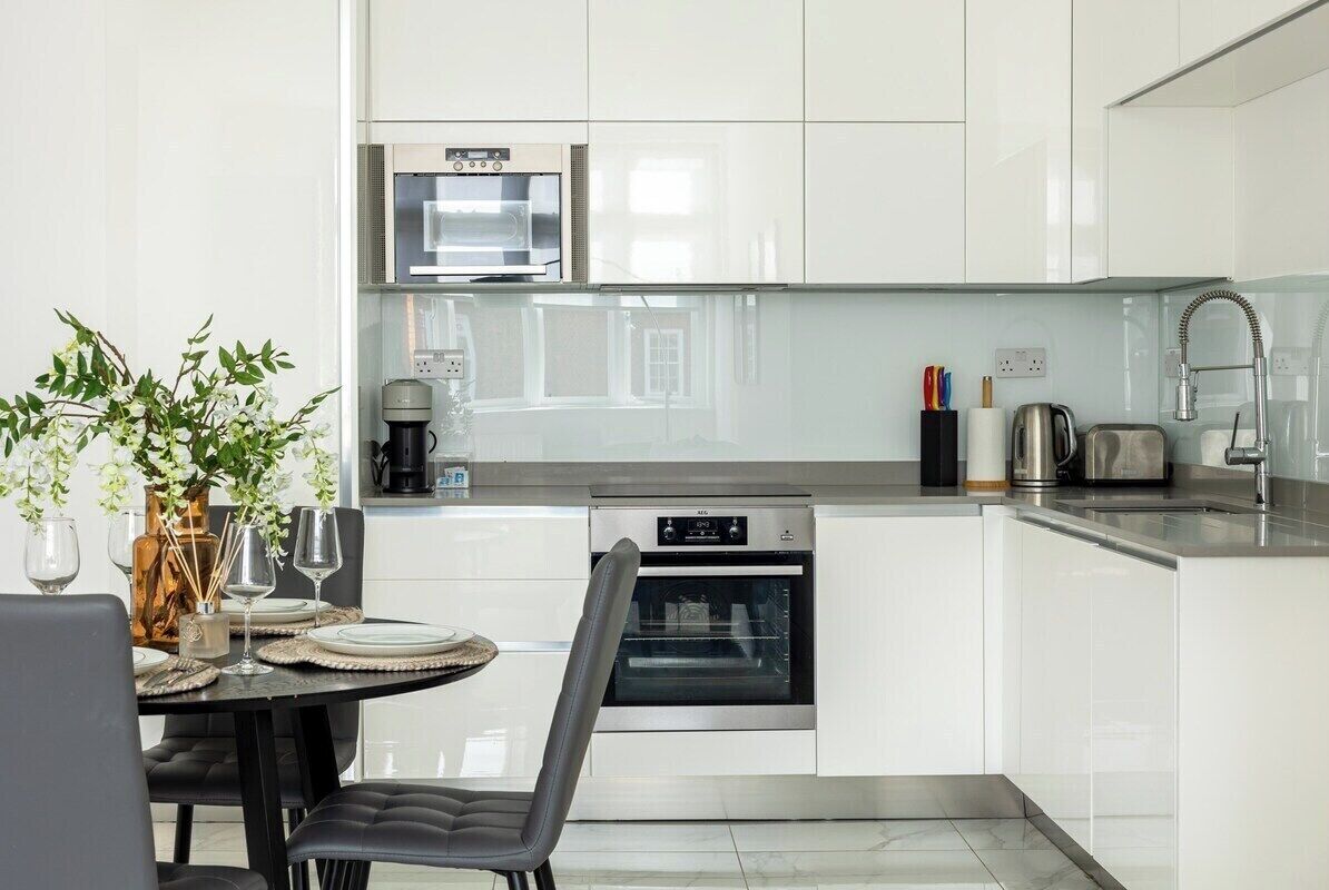 Una cocina moderna con armarios blancos, horno empotrado, microondas y cafetera.