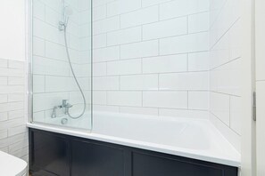 A modern bathroom with a glass-enclosed shower, a white bathtub, and black cabinetry.