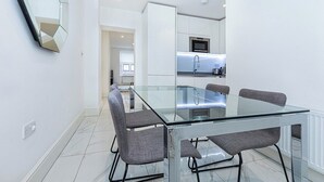 A modern kitchen with a glass dining table and four grey chairs. - Modern Flat, Steps from Oxford Street! (London)