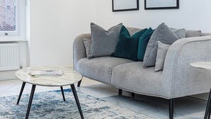 A modern living room with a grey sofa, a round coffee table, and a blue patterned rug. - Modern Flat, Steps from Oxford Street! (London)