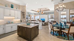 A spacious kitchen with a large island, white cabinetry, and a dining area with a glass table and chairs. - Stunning Gulf waterfront pool and spa home (Marco Island)