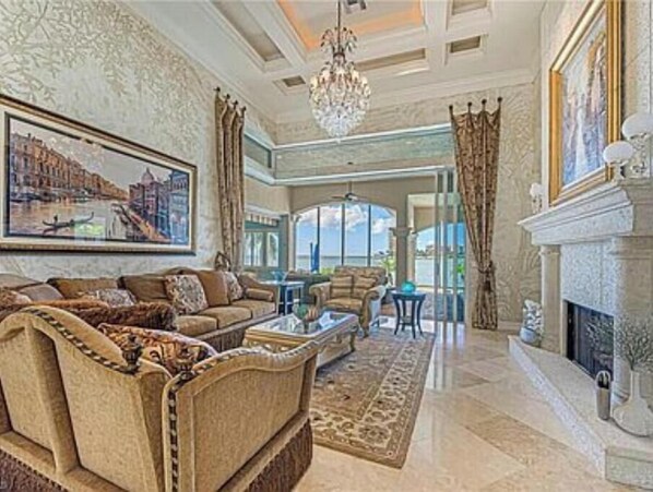 A spacious living room with a large painting, a fireplace, and a view of the outdoors. - Stunning Gulf waterfront pool and spa home (Marco Island)