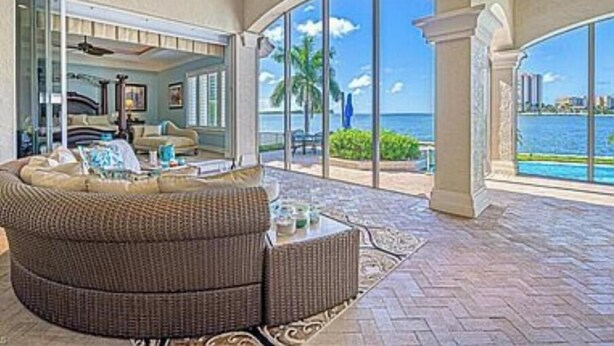 A spacious living area with a large, curved sofa, a ceiling fan, and a view of the ocean through large windows. - Stunning Gulf waterfront pool and spa home (Marco Island)