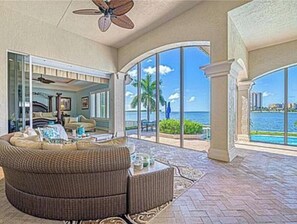 A spacious living area with a large, curved sofa, a ceiling fan, and a view of the ocean through large windows. - Stunning Gulf waterfront pool and spa home (Marco Island)
