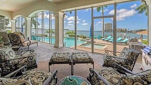 A spacious room with a large glass door leading to a pool area, featuring outdoor seating and a view of the ocean. - Stunning Gulf waterfront pool and spa home (Marco Island)