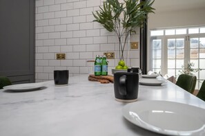 A modern kitchen with white subway tiles, a marble countertop, and a dining area with a table set for two. - Host Stay Olde Place Cottage (Brighton)