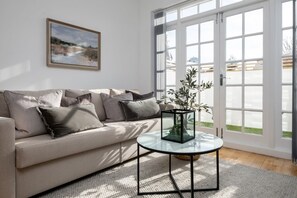 Ett vardagsrum med en beige soffa, ett soffbord i glas och en krukväxt.