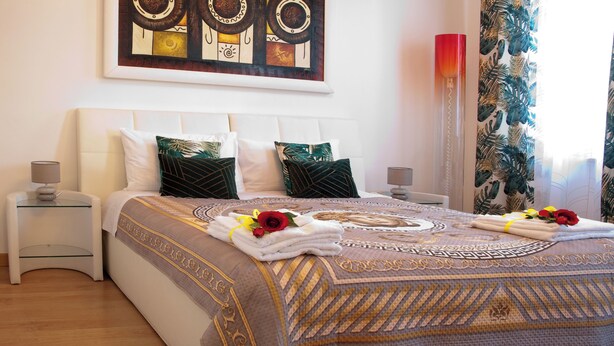 A neatly made bed with a patterned bedspread, two pillows, and a decorative headboard. - ARENA AROUND - PRESTIGE SUITE (Verona)