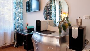 A modern room with a desk, a flat-screen TV, a large mirror, and a water dispenser. - ARENA AROUND - PRESTIGE SUITE (Verona)