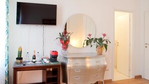 A room with a wooden desk, a mirror, a television mounted on the wall, and a door. - ARENA AROUND - PRESTIGE SUITE (Verona)
