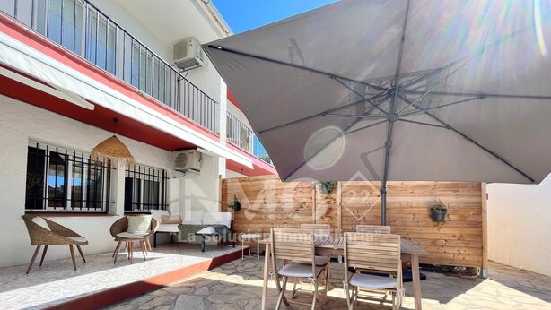 Une terrasse avec un sol en pierre, des meubles en bois et un grand parasol.