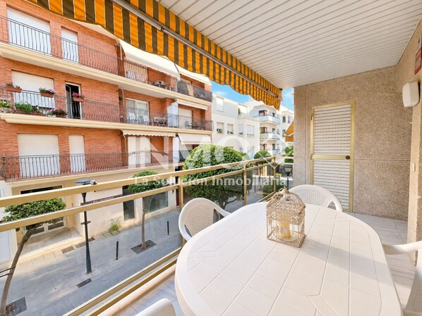 A balcony with a table and chairs, a lantern, and a view of neighboring buildings.