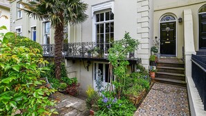 A traditional two-story building with a balcony, a small garden with various plants, and a tiled pathway leading to the entrance. - Host Stay Hanover Rest (Brighton)