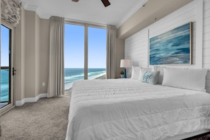 A bedroom with a large bed, a view of the ocean, and a painting on the wall.