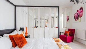 A bedroom with a large bed, white walls, a mirror, a pink chair, and a flower painting. - Host Stay Montpelier Sanctuary (Brighton)