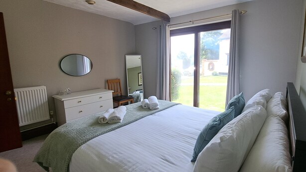 A bedroom with a bed, a dresser, a mirror, and a window with curtains. - Cozy 1 bed with countryside views near Peterborough (Yaxley)