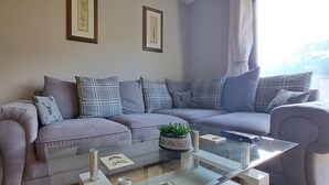 A modern living room with a grey sofa set, a glass coffee table, and two framed pictures on the wall. - Cozy 1 bed with countryside views near Peterborough (Yaxley)