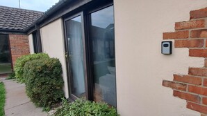 A house with a sliding glass door, a brick wall, and a small green bush. - Cozy 1 bed with countryside views near Peterborough (Yaxley)