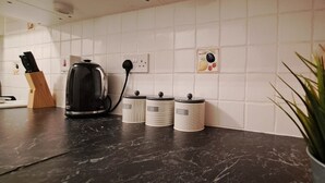 A kitchen with a black countertop, a coffee maker, and three containers labeled tea, coffee, and sugar. - Cozy 1 bed with countryside views near Peterborough (Yaxley)