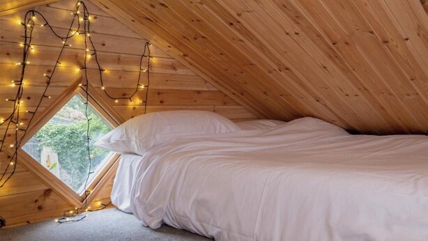 A cozy attic bedroom with a sloped ceiling, a bed, and string lights. - Host Stay The Eco Cabin (Brighton)