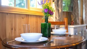 A wooden dining table with a green vase of flowers, white bowls, and cutlery. - Host Stay The Eco Cabin (Brighton)