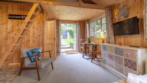 A wooden cabin interior with a staircase, a television mounted on the wall, a small table, and a sofa. - Host Stay The Eco Cabin (Brighton)