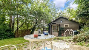 A small wooden cabin with a window and a door, surrounded by lush greenery. - Host Stay The Eco Cabin (Brighton)