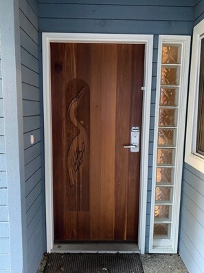 Une porte en bois ornée d’un motif d’oiseau sculpté, une sonnette blanche et un panneau de verre réfléchissant.