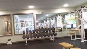 Un gimnasio con equipo de ejercicio, espejos y un banco.