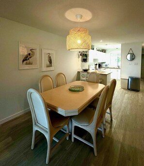 A dining area with a wooden table and white chairs, a hanging light fixture, and wall-mounted artwork.
