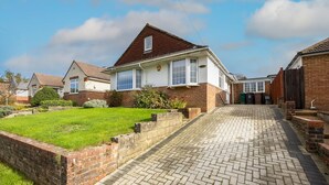 A residential house with a paved driveway leading to the front door, surrounded by a well-maintained lawn and a brick wall. - Host Stay Downs Valley House (Brighton)