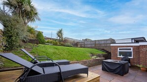 A patio with two lounge chairs and a table, surrounded by a brick wall and greenery. - Host Stay Downs Valley House (Brighton)