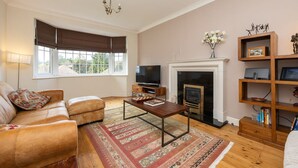 A living room with a sofa, a television, a fireplace, and a bookshelf. - Host Stay Downs Valley House (Brighton)
