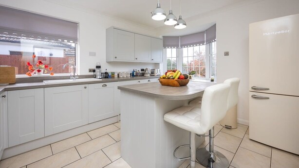 A modern kitchen with white cabinetry, a central island with a fruit bowl, and a refrigerator labeled "Montpellier". - Host Stay Downs Valley House (Brighton)