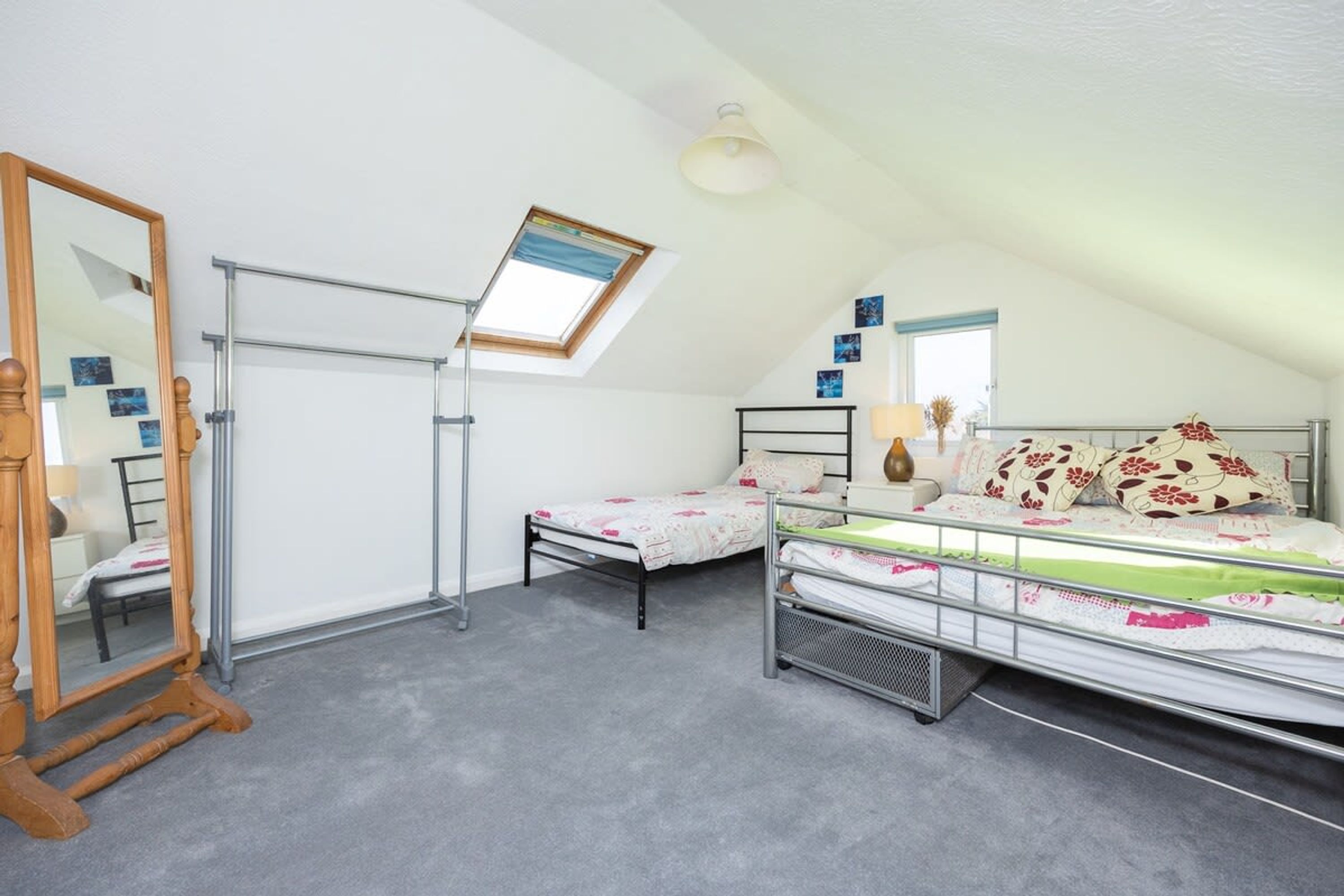 A bedroom with a skylight, a bed with floral bedding, a bedside table with a lamp, and a wooden dresser.