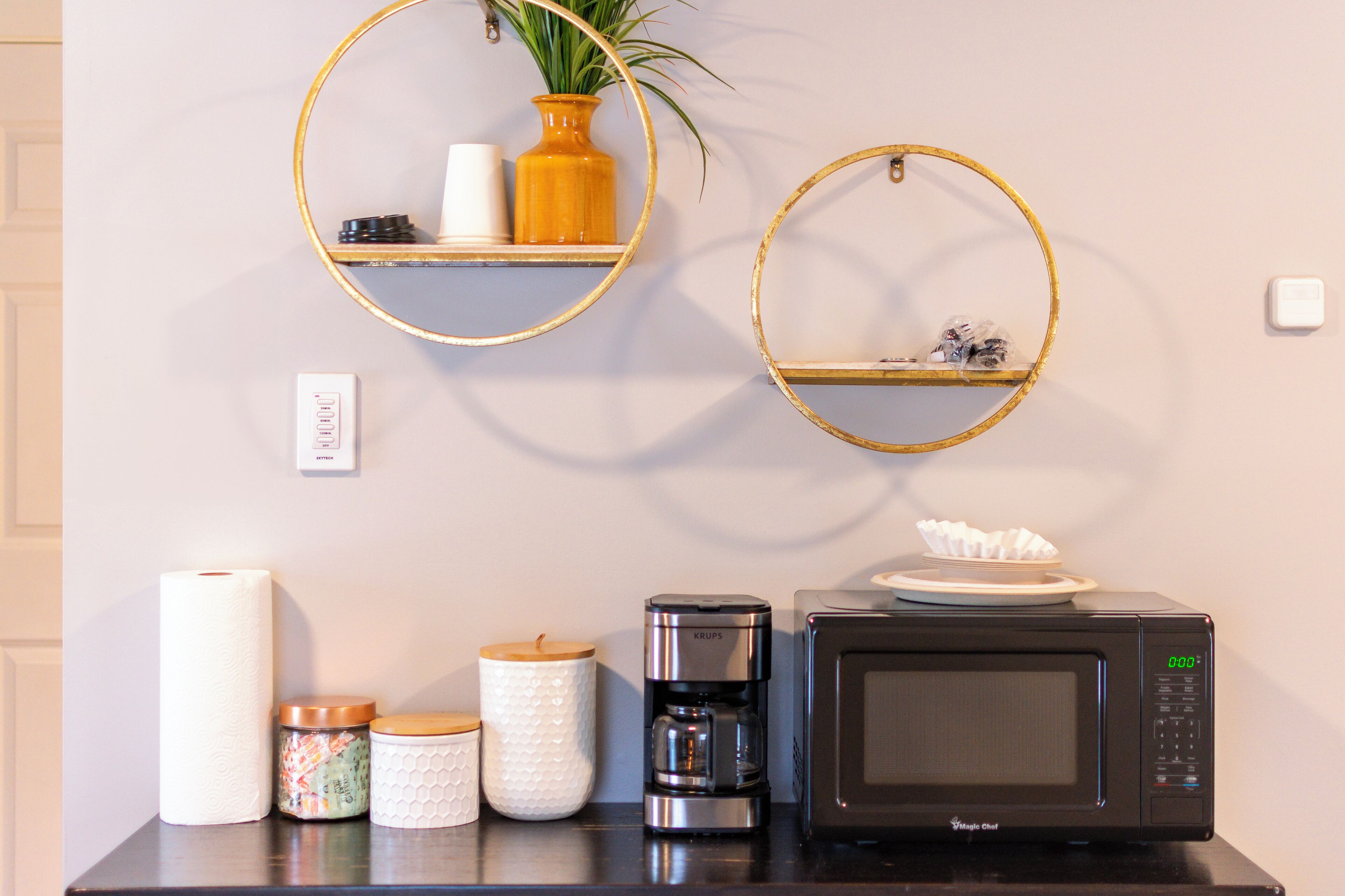 Una encimera de cocina con microondas, cafetera y frascos de almacenamiento.