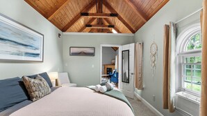 A bedroom with a large bed, a ceiling fan, a window with curtains, and a door leading to another room. - TuckAway Suites at East Branch (Intervale)